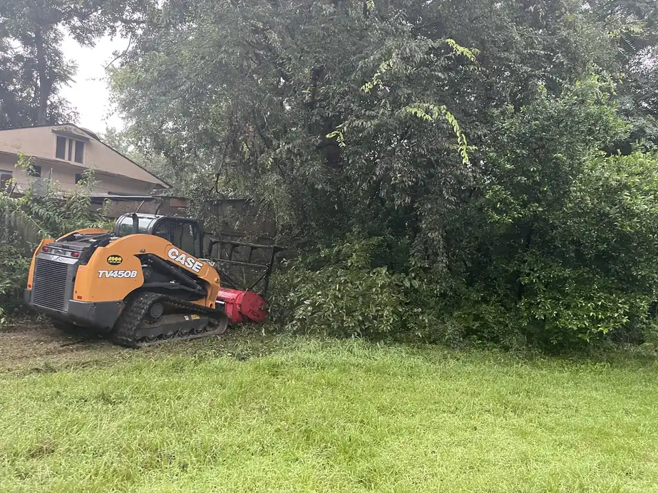 Orange CASE track loader with a red forestry mulcher clearing overgrowth behind a house