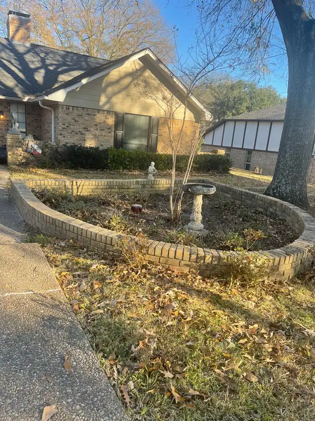 Curved brick flower bed cleared down to soil with the birdbath left in place